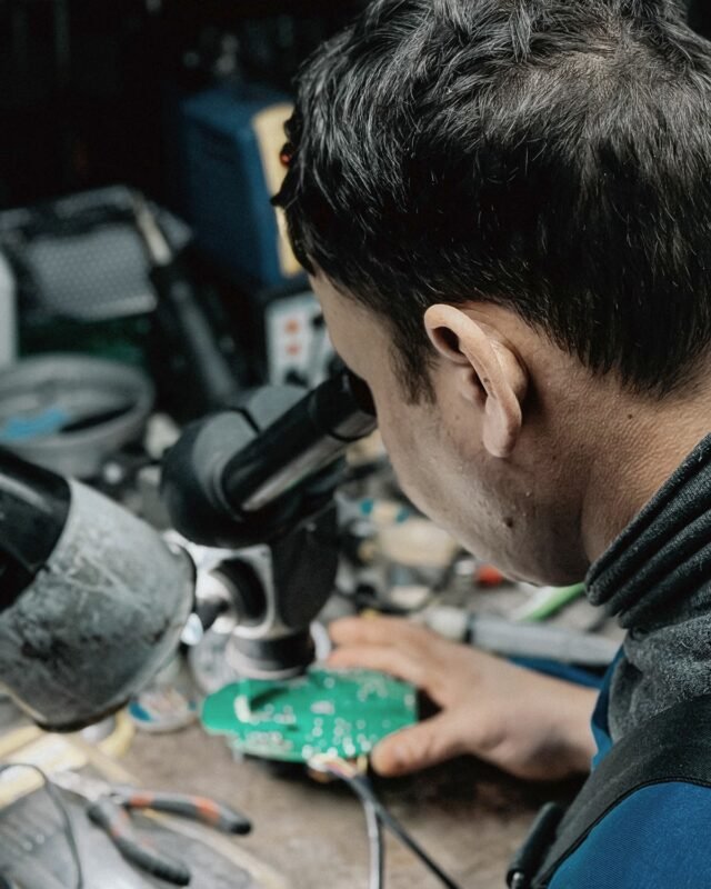 Technician inspecting a printed circuit board under a microscope
